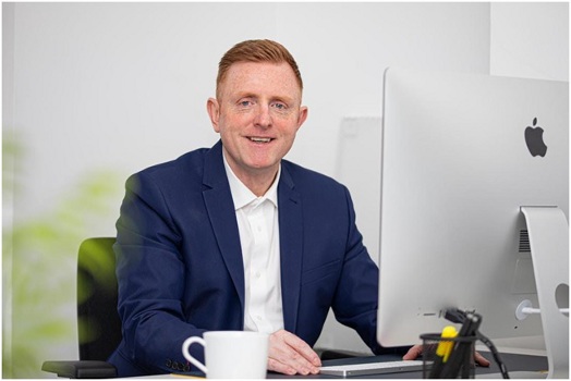 Businessman in a blue suit sitting at a desk smiling at the camera after implementing content networking for a contractor business